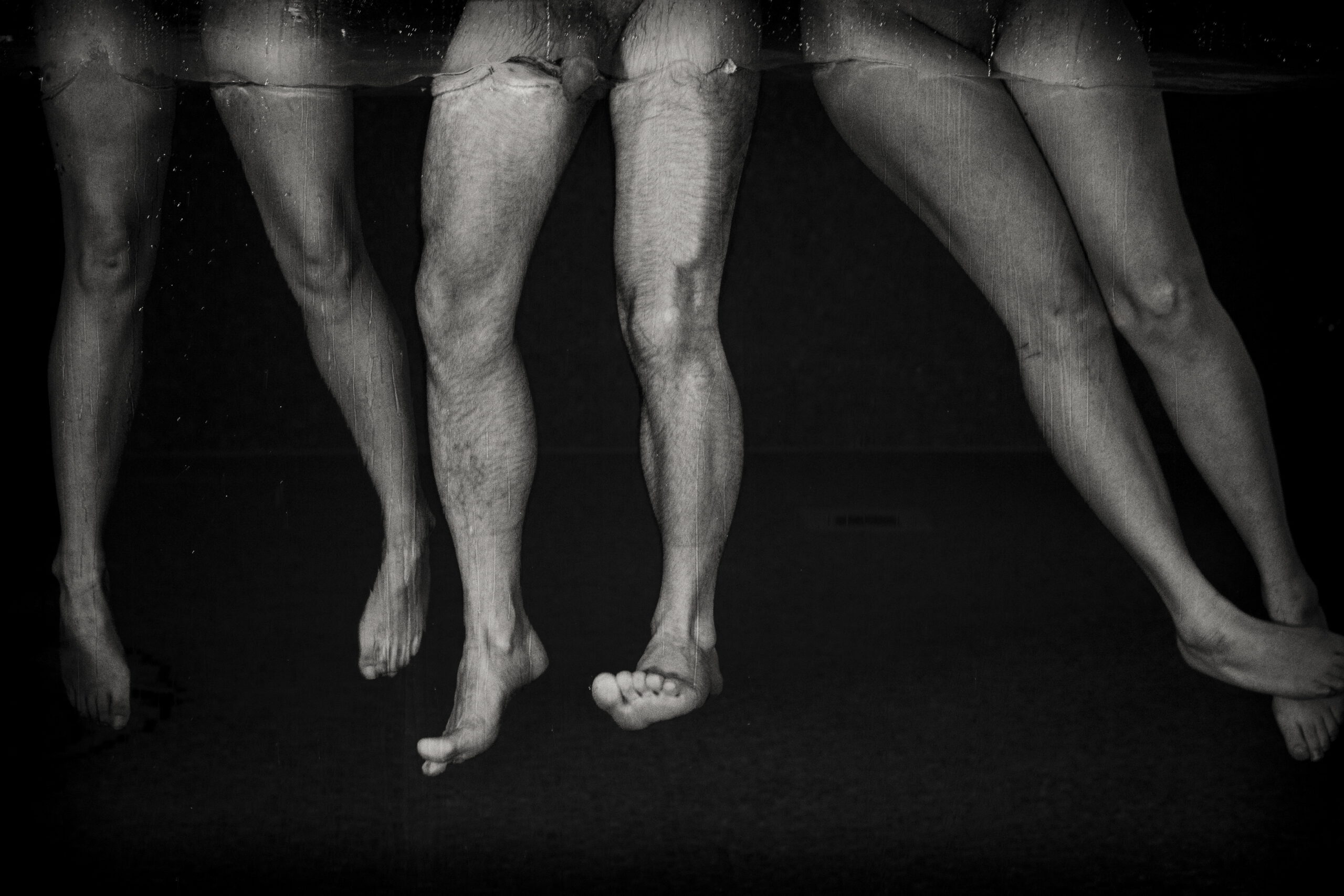 Fine art black-and-white photograph of submerged legs hovering beneath the water’s surface, by Menno van der Meulen