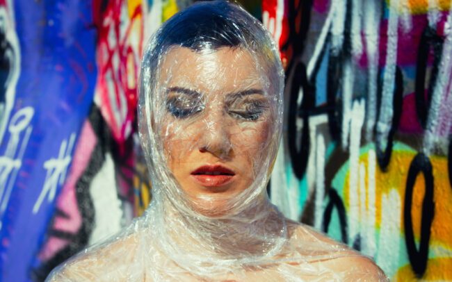 Fine-art portrait of Catherine wrapped in a translucent veil against a vivid graffiti wall — by Menno van der Meulen.