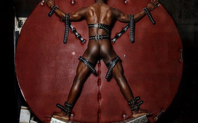 Male figure restrained against a red circular support, photographed by Menno van der Meulen in 