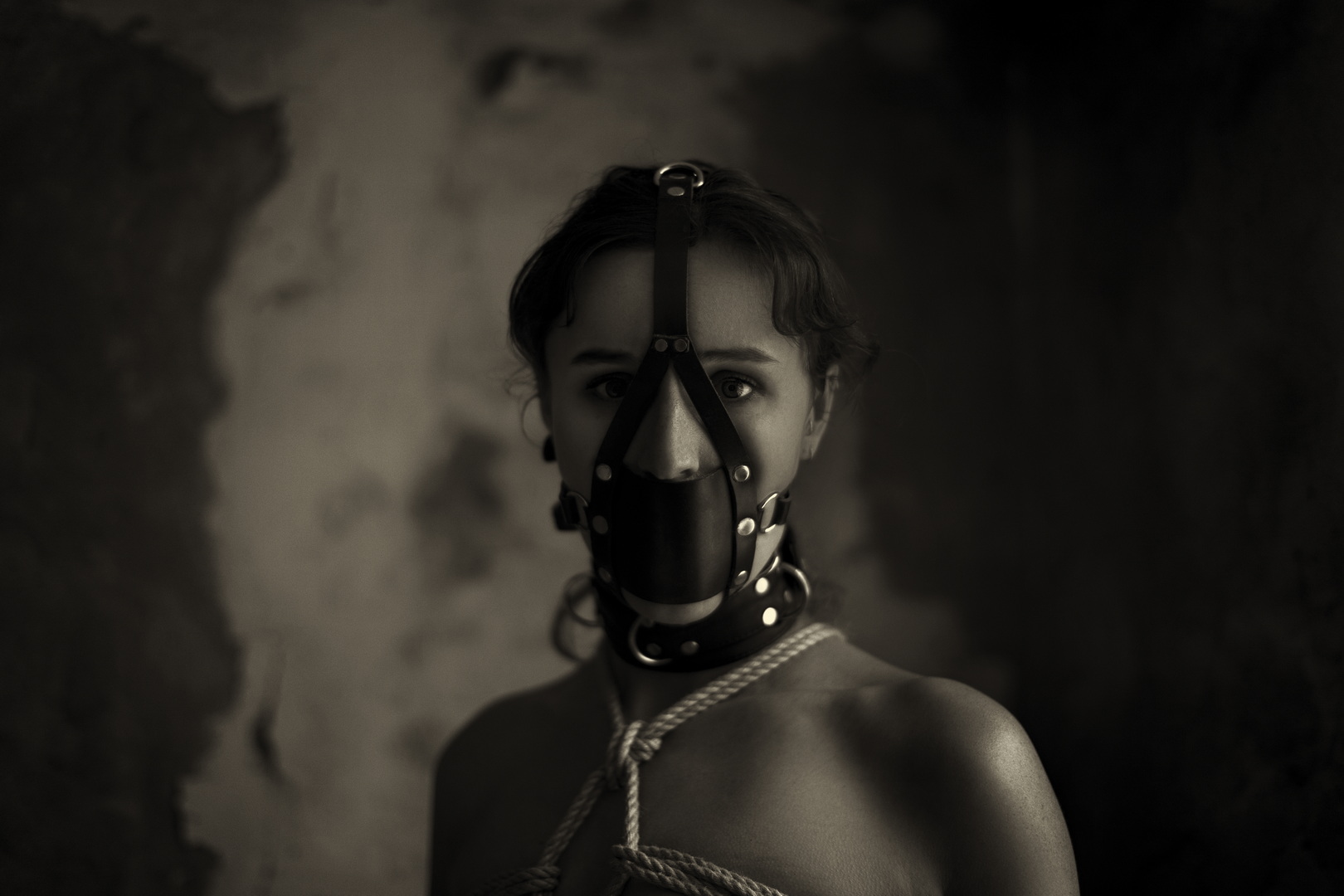 Fine art black-and-white portrait of a woman wearing a leather muzzle mask and collar, intense eyes and moody light — by Menno van der Meulen.