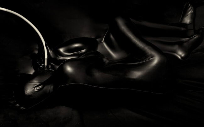 Fine art photography: suspended human form encased in vacuum latex, abstract contours, moody studio lighting.