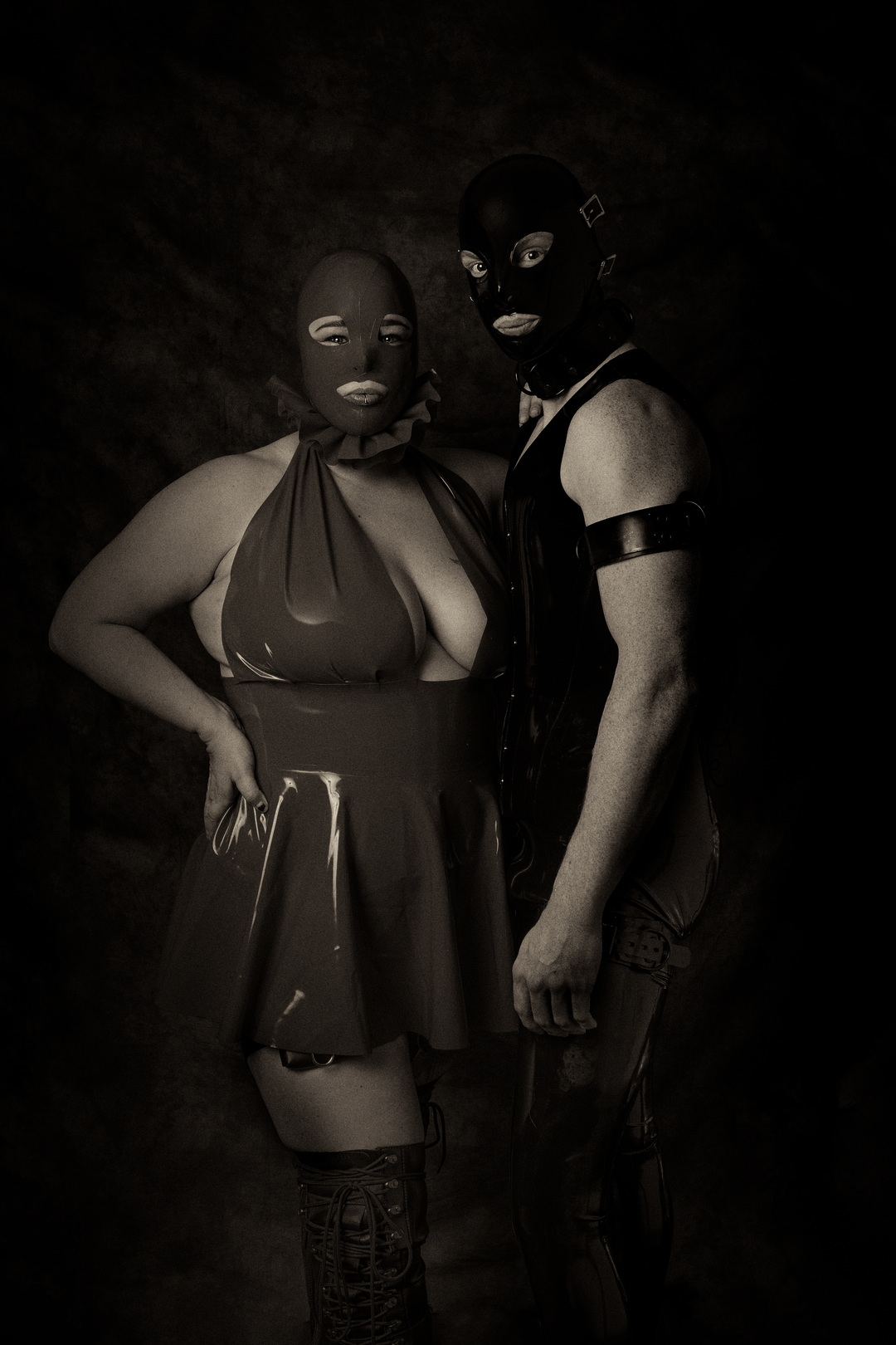 Two masked figures standing together in a studio, wearing dark clothing and looking toward the camera.